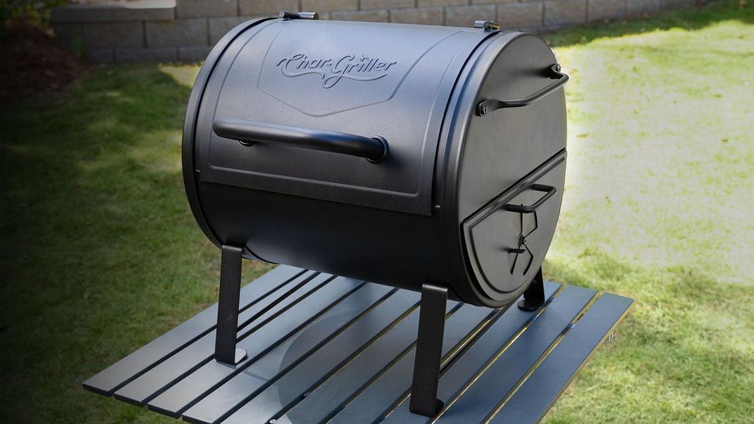 A small black barrel grill sits on top of a table outside on a lawn