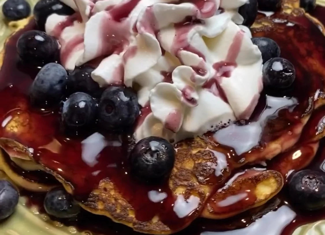 Cheesecake pancakes covered with fresh blueberries, whipped cream, and bluebarry syrup
