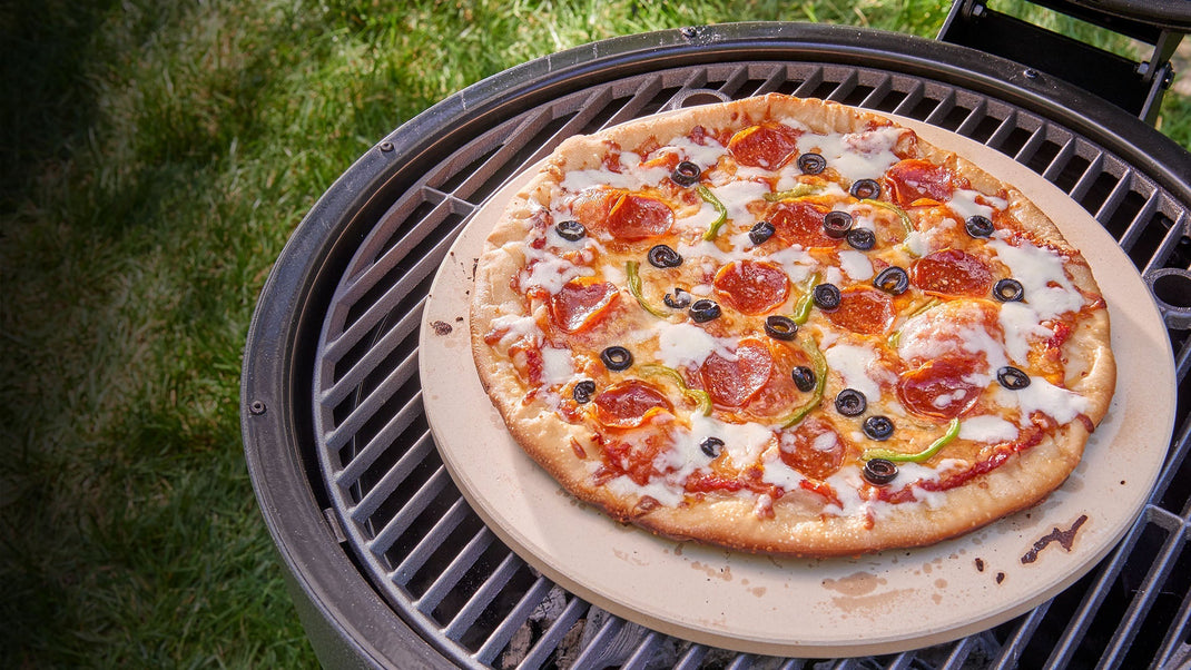 A pizza bakes on a pizza stone set on the grate of an AKORN kamado grill