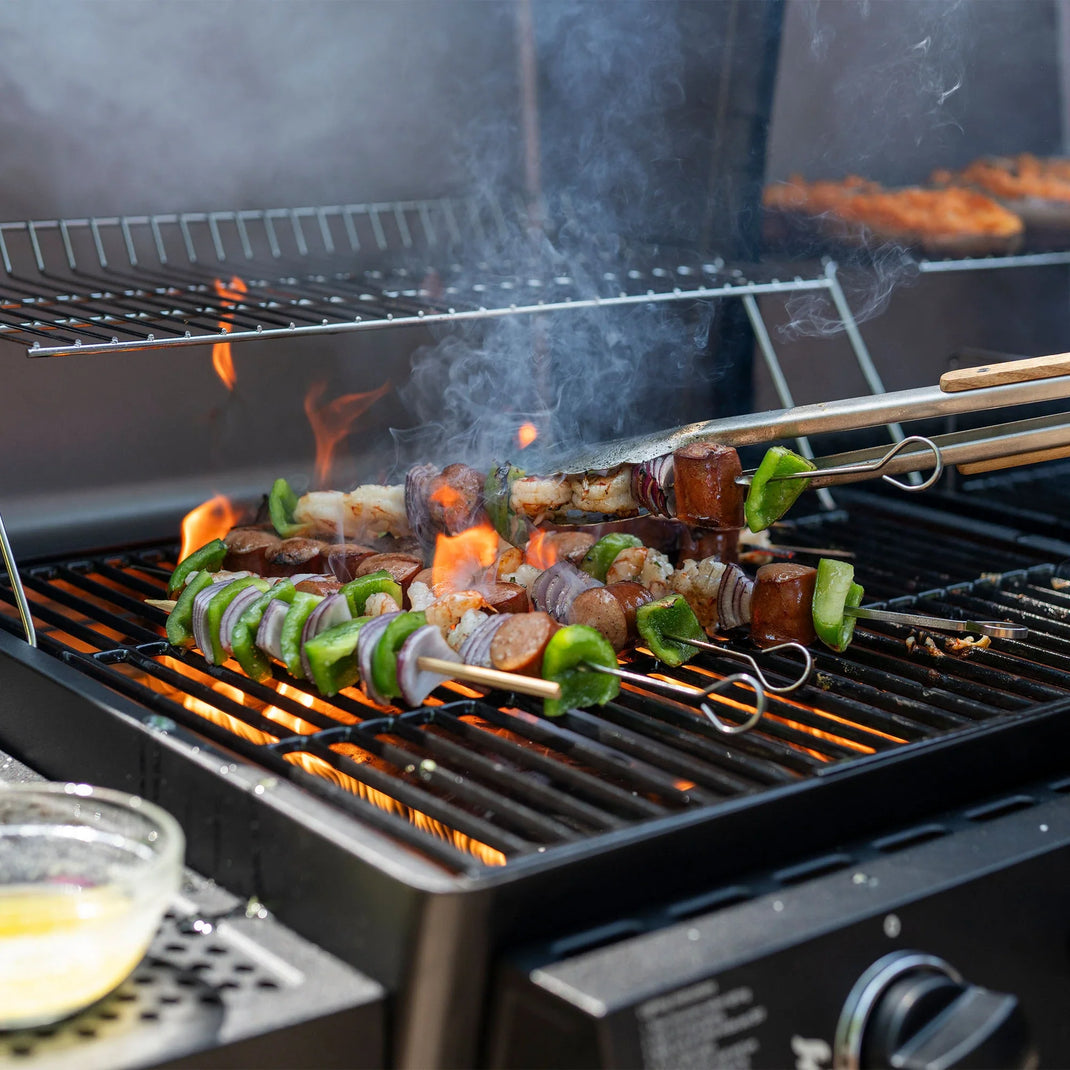 Skewers of peppers, onion, and sausage cooking on the gas side of the grill. 