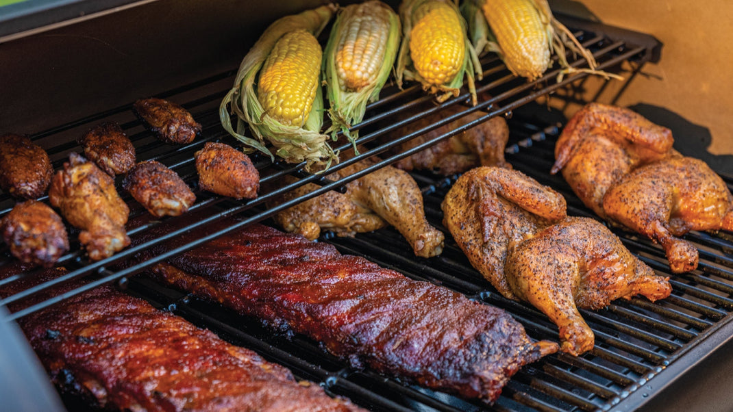 Corn on the cob, wings, racks of ribs, and half chickens cook on a grill