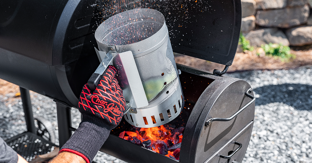 A charcoal chimney being used to dump charcoal into the fire by strong man.