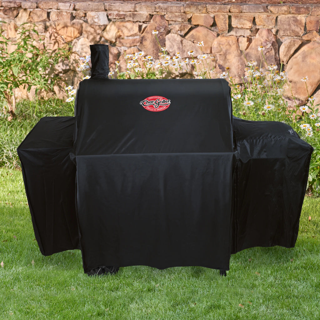 A covered grill outside on a lawn, in front of a bed of daisies and a rock wall.