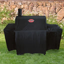 A covered grill outside on a lawn, in front of a bed of daisies and a rock wall.