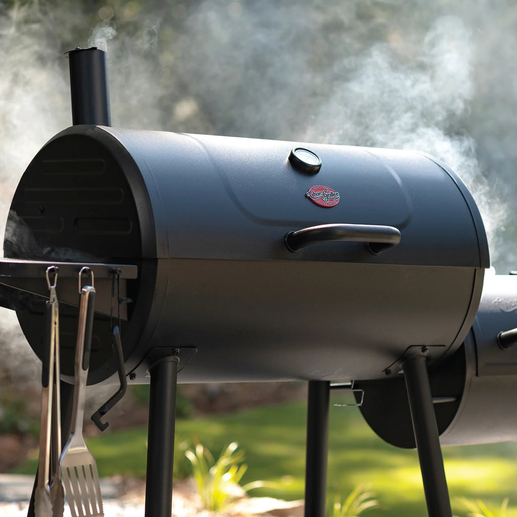 A closed Smokin' Champ with smoke coming out from the chimney on the left of the barrel grill and around the edges of the grill lids. 