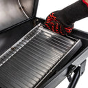 A person wearing a grilling glove removes the EasyDump Ash Pan from the bottom of the grill body.