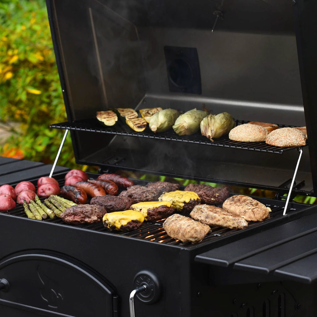 Open traditional charcoal grill cooking burgers, chicken breasts, sausages, and a variety of vegetables.
