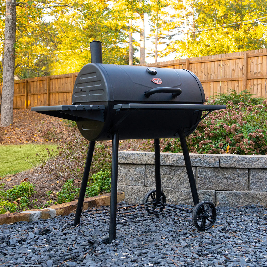 Super Pro grill outside on a black rock patio in front of a retaining wall, landscaped yard, and wooden fence.
