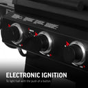 Closeup of 3 burner control knobs on the front panel of a Texas Trio grill. An igniter button is placed between the 2 leftmost knobs. Text overlay reads: Electronic ignition to light fuel with the push of a button.