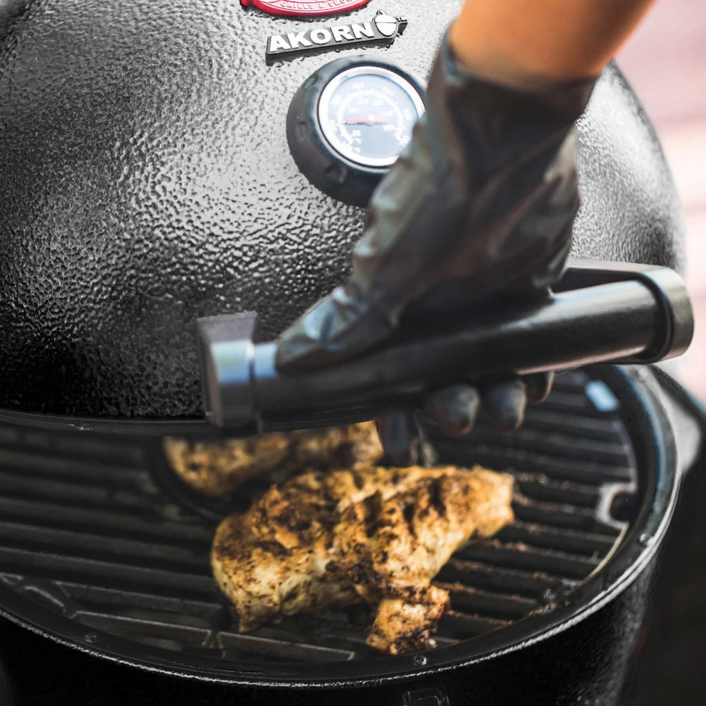 Someone opens a black AKORN Jr. grill to show 2 chicken breasts cooking inside.