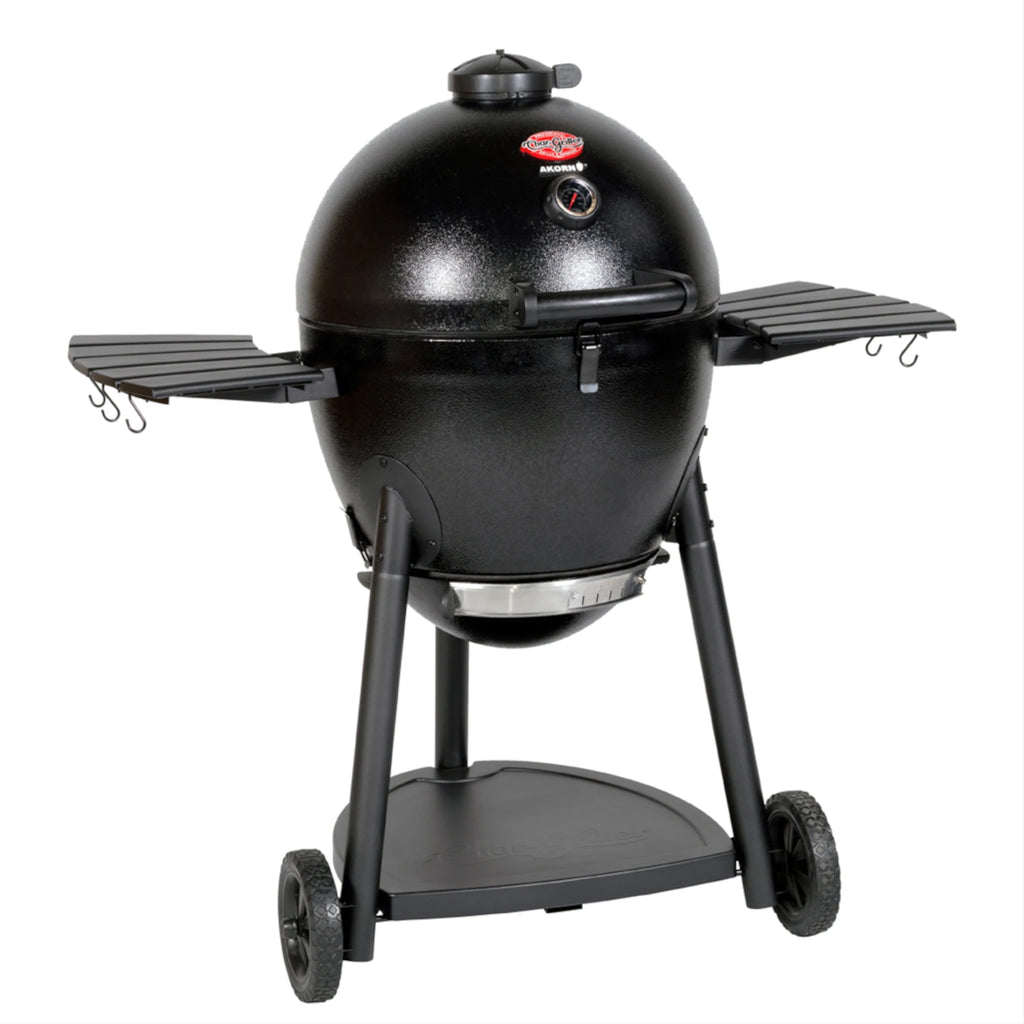 Angled view of the black AKORN kamado grill mounted on a wheeled cart with side shelves up against a white background.