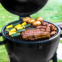 Closeup of meats and vegetables cooking on a black AKORN grill. The cooking grate has the Char-Griller logo in the center of it.