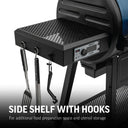 Closeup of the perforated metal side shelf of a Gravity Fed 980 grill. The shelf is mounted on the left side of the grill body. The digital control panel is mounted under the front of the shelf. 3 utensil hook are mounted on the outside edge of the shelf. Text overlay reads: Side shelf with hooks for additional food preparation space and utensil storage.