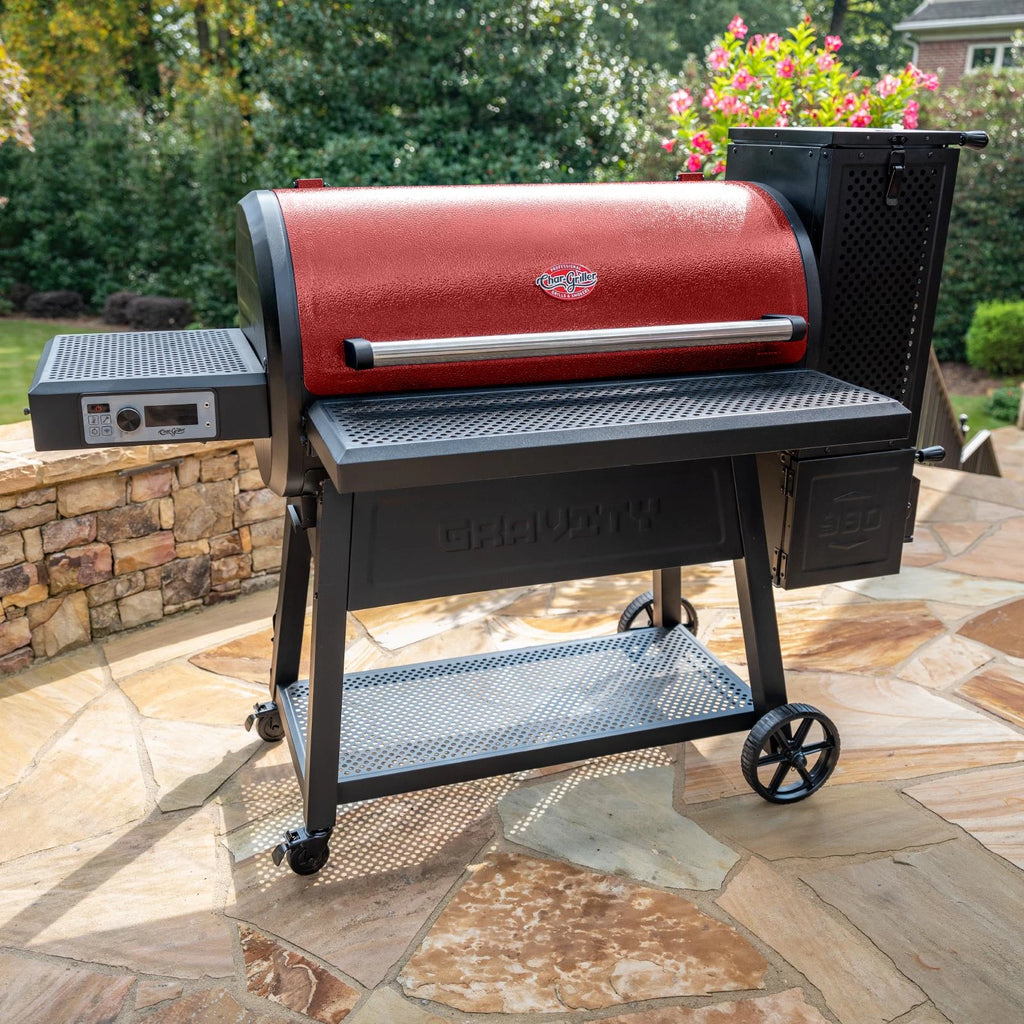 Red Gravity Fed 980 grill on a stone paved patio in front of a low stone wall. The charcoal hopper is on the right. The control panel is beneath the side shelf on the left.