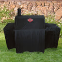 A covered grill outside on a lawn, in front of a bed of daisies and a rock wall.