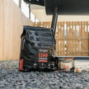 Bag of Char-Griller lump charcoal and a box of Char-Griller fire starters sit on the ground by the leg of a Char-Griller barrel grill