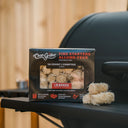 Box of Char-Griller fire starters on the front shelf of a Char-Griller barrel grill with a wooden fence in the background