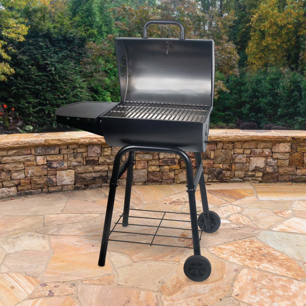 Open King-Griller Gambler charcoal grill on wheels in an outdoor setting with stone patio and greenery.
