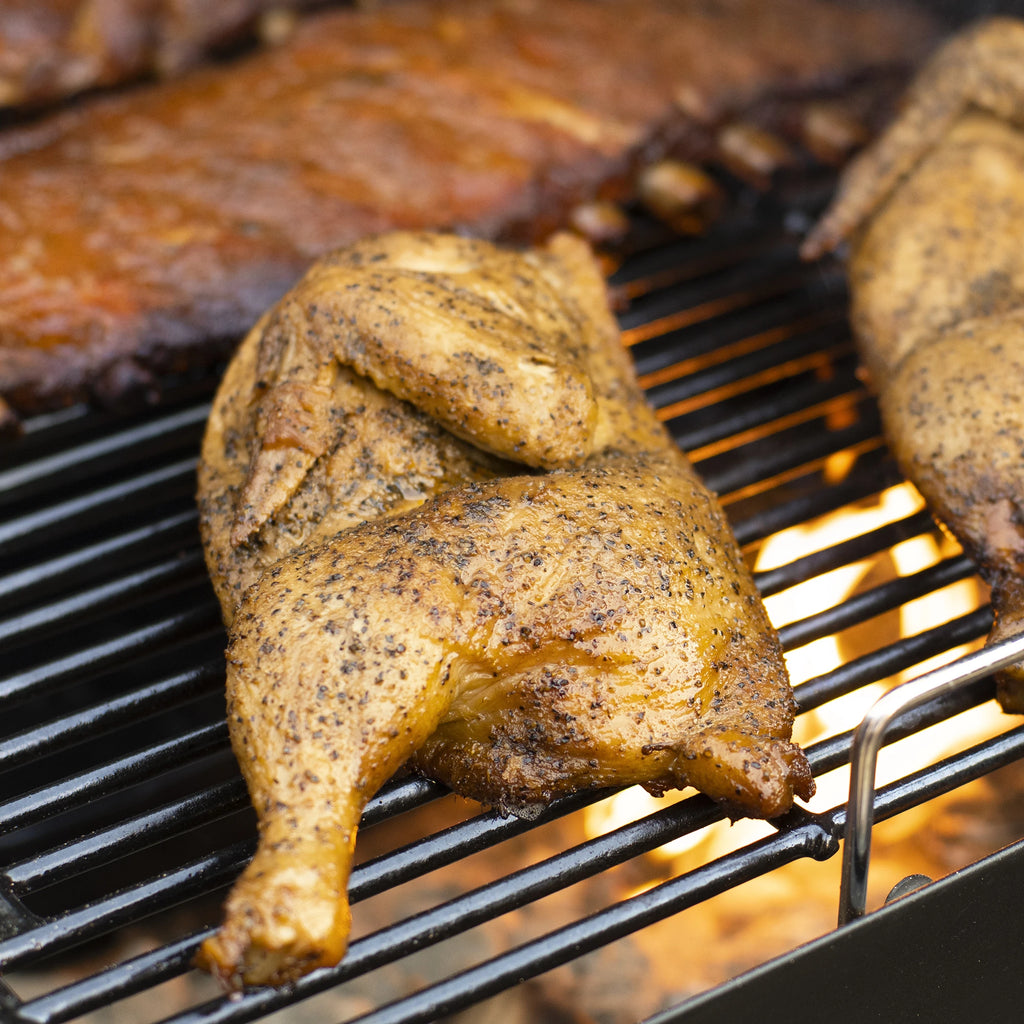 Chicken halves and racks of ribs cook over charcoal. 