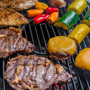 Grilled steak, chicken breast, zucchini, yellow squash, red and orange sweet peppers, and cheese-topped burgers cooking on a black grill grate.