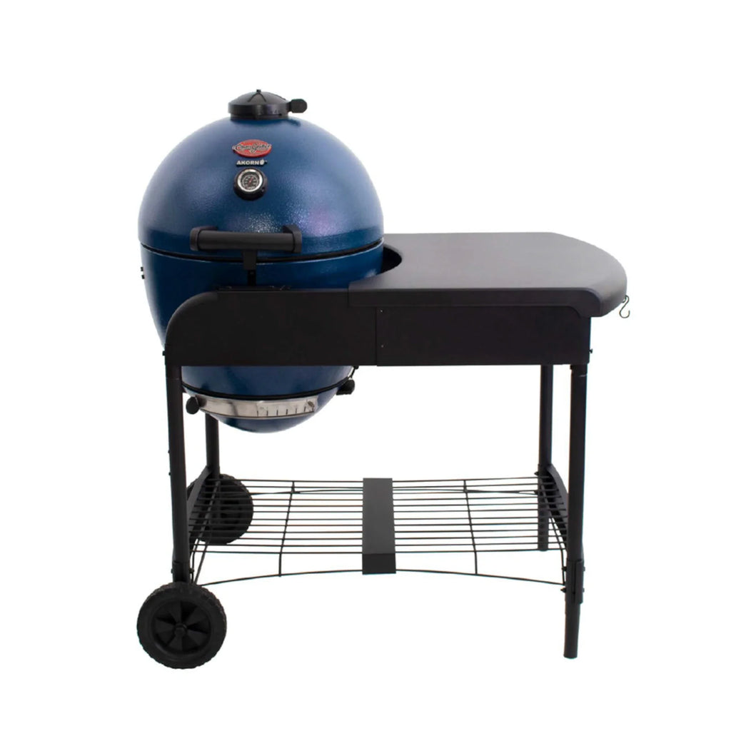 A sapphire blue Akorn kamado grill in a cart that has a black side table, 2 wheels on the left side under the grill, and a wire shelf between the cart legs. Shown on a solid white background.