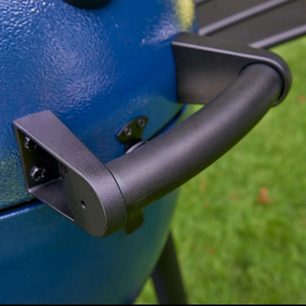 Close-up of a black handle attached to a blue grill lid, with green grass blurred in the background.