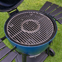 A blue and black kamado-style outdoor grill with a circular cast-iron grate and black side shelves, shown from above on a green grass lawn.