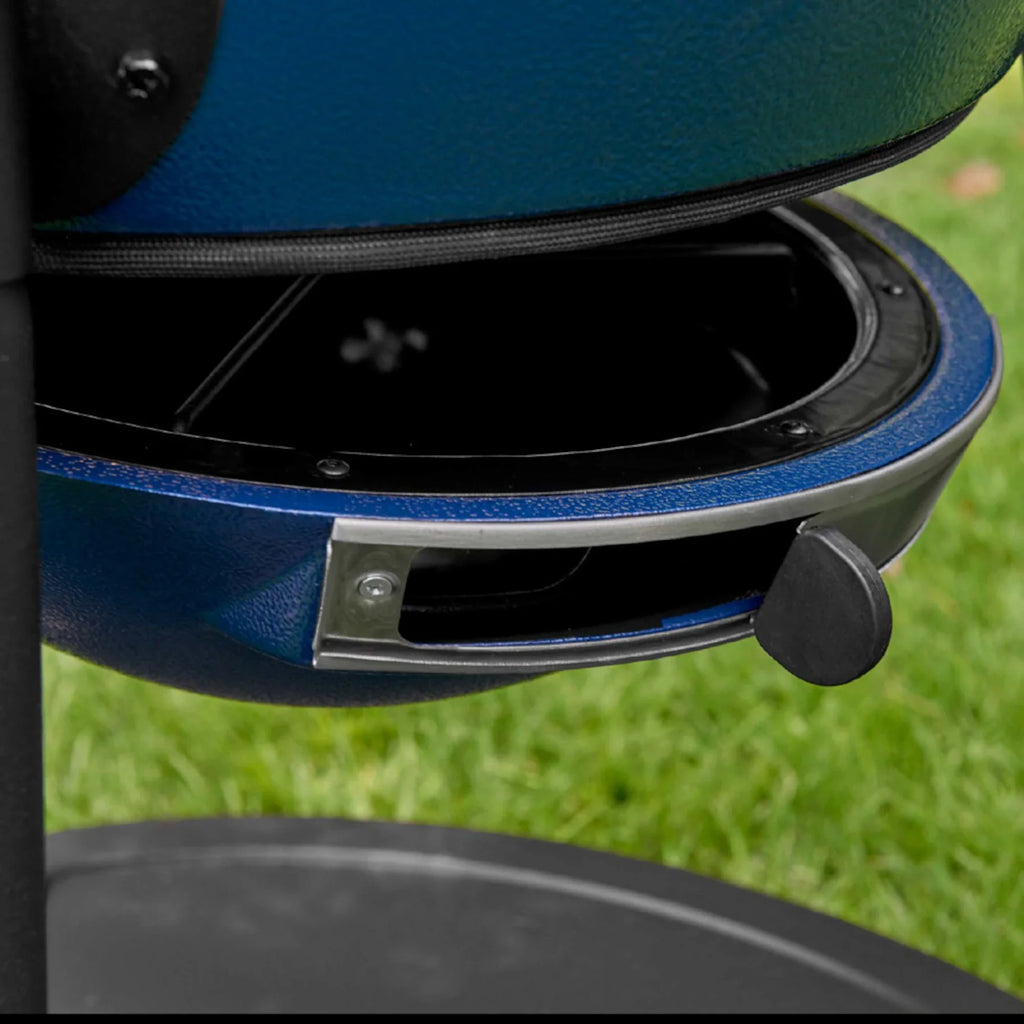 Close-up of a blue outdoor grill base with an adjustable air vent, set against a blurred green grass background.
