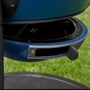 Close-up of a blue outdoor grill base with an adjustable air vent, set against a blurred green grass background.