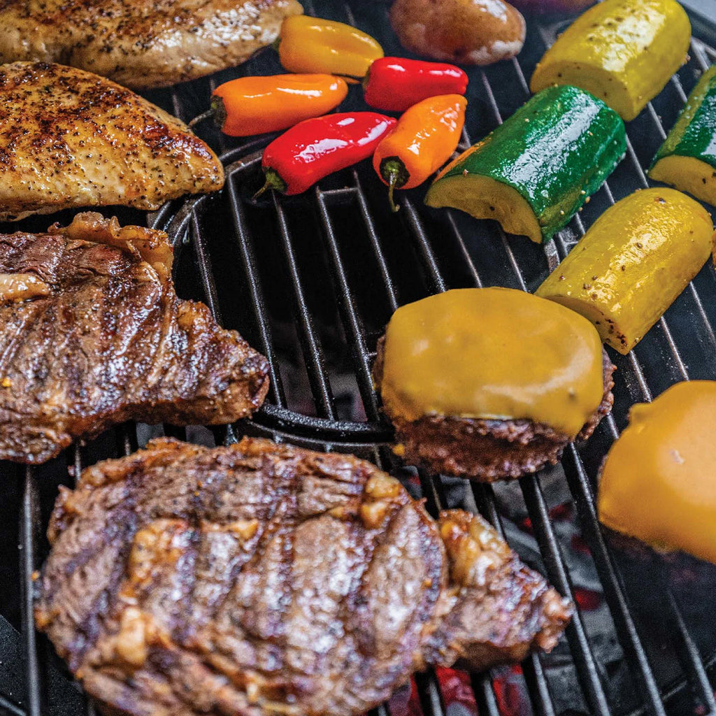 Grilled steak, chicken breast, zucchini, yellow squash, red and orange sweet peppers, and cheese-topped burgers cooking on a black grill grate.