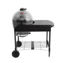 A ash grey Akorn kamado grill in a cart that has a black side table, 2 wheels on the left side under the grill, and a wire shelf between the cart legs. Shown on a solid white background.