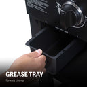 Closeup of someone sliding the removable grease cup out from under the front left side of the griddle. Text reads: Grease tray for easy cleanup.