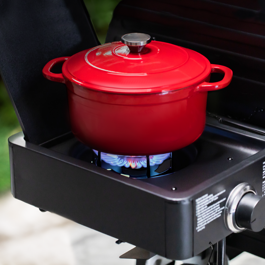 A bright red dutch oven sits above the flame of the side burner.