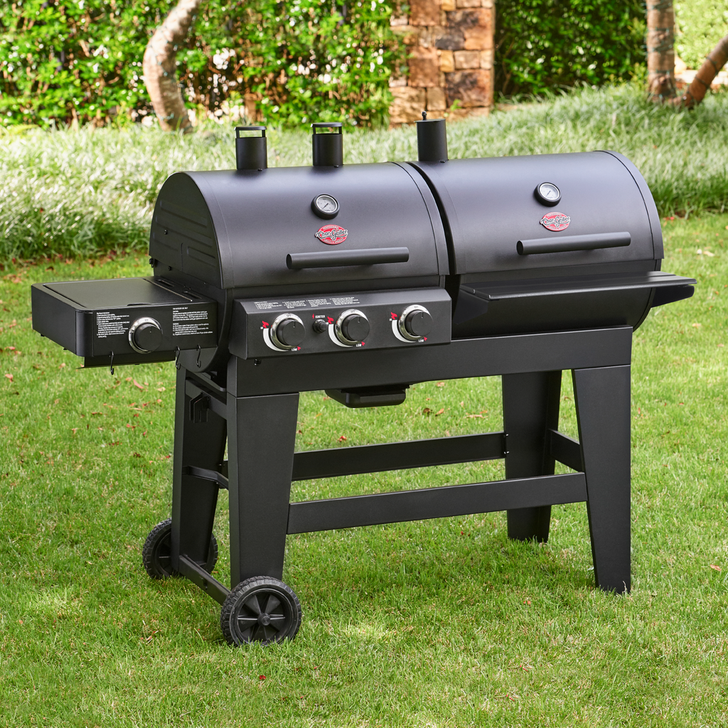 A Double Play grill sitting outside in a grassy area. Small trees in a bed of monkey grass are behind the grill.
