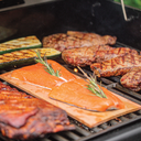 Steaks, a rack of ribs, zucchini halves, and salmon filets on a wooden plank all cook on the grill's cooking grate