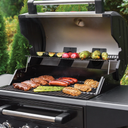 An open Flavor Pro grill showing vegetables on the warming rack and steaks, chicken breasts, sausages, and asparagus on the main cooking grate.